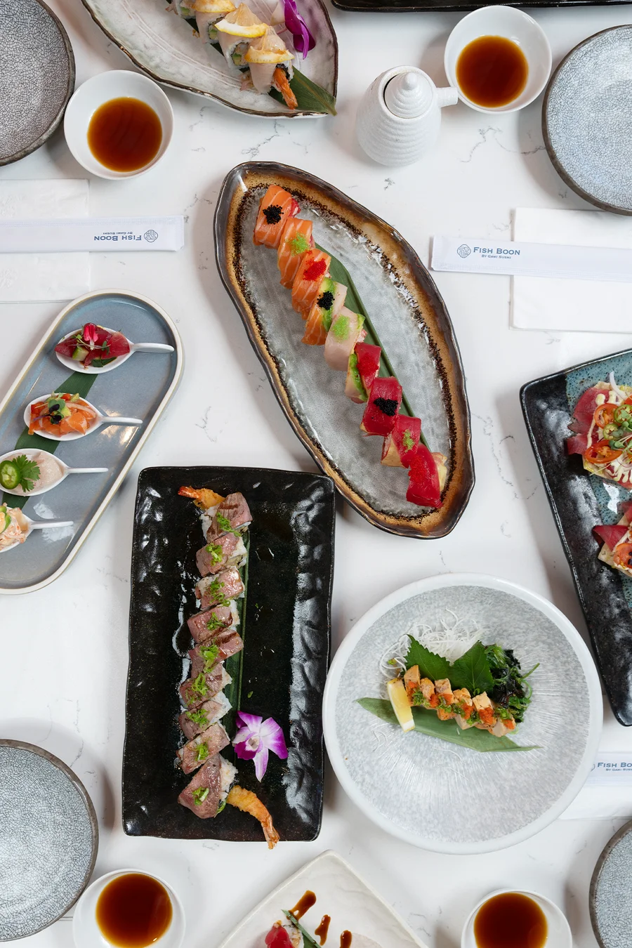 An overhead spread of plated sushi and rolls with Fish Boon branded chopstick sleeves.